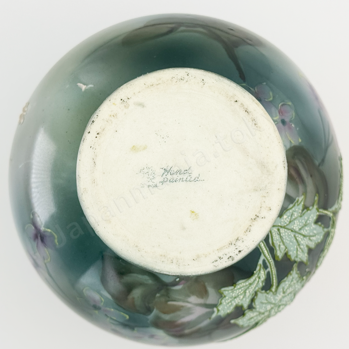 Back stamps: Maple Leaf  Japanese old fine china. Old Noritake.
This exquisite and captivating piece showcases polychrome and Moriage decoration, featuring delicate white flowers tinged with soft pink and leaves outlined in green. The upper and lower portions are finished in a smoky green, while the center glows with a radiant brightness, as though illuminated by light. The elegantly small mouth of the base, complemented by graceful handles on both sides, adds to its charm and timeless appeal.